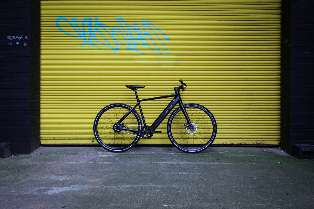 Falcon Zone Electric Hybrid Bike - single speed city bike against a yellow shutter — view 31